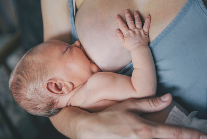 Baby ved brystet, det andet bryst er dækket af ammeBH og ammetop